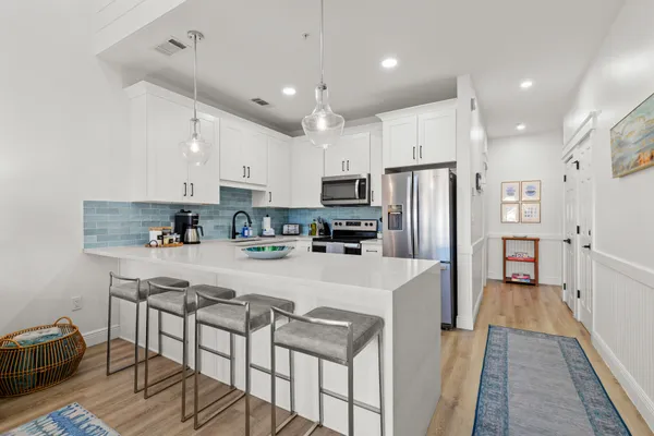 a large kitchen with stainless steel appliances a refrigerator a stove top oven a sink dishwasher and white cabinets with wooden floor
