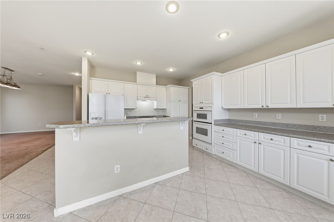 3766 Port Ritchey Street Las Vegas, NV 89147 - Photo 16 of 50 Kitchen with white cabinetry, white appliances, a breakfast bar, light tile patterned floors, and grey granite counters