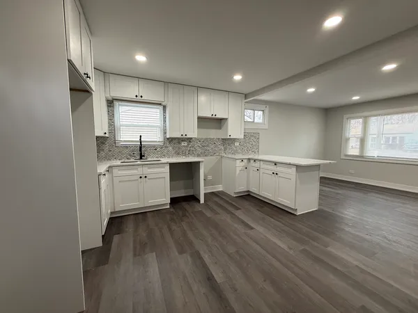 a large white kitchen with a sink dishwasher a stove and white cabinets with wooden floor