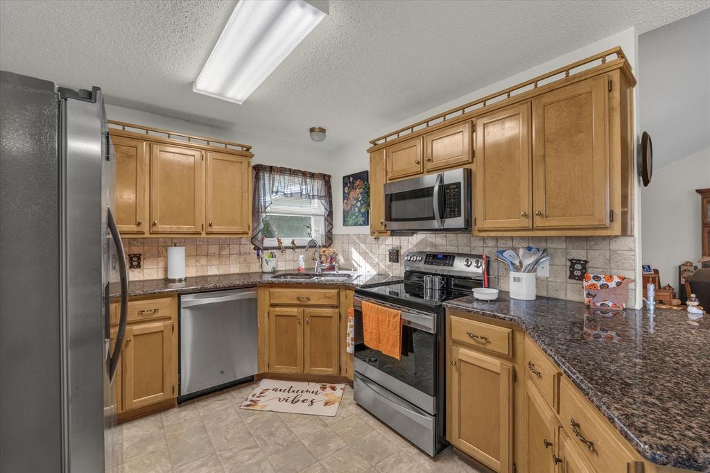 107 Fort Graham Circle Waco, TX 76705 - Photo 11 of 40 Kitchen featuring stainless steel appliances, tasteful backsplash, a textured ceiling, brown cabinets, and dark stone counters
