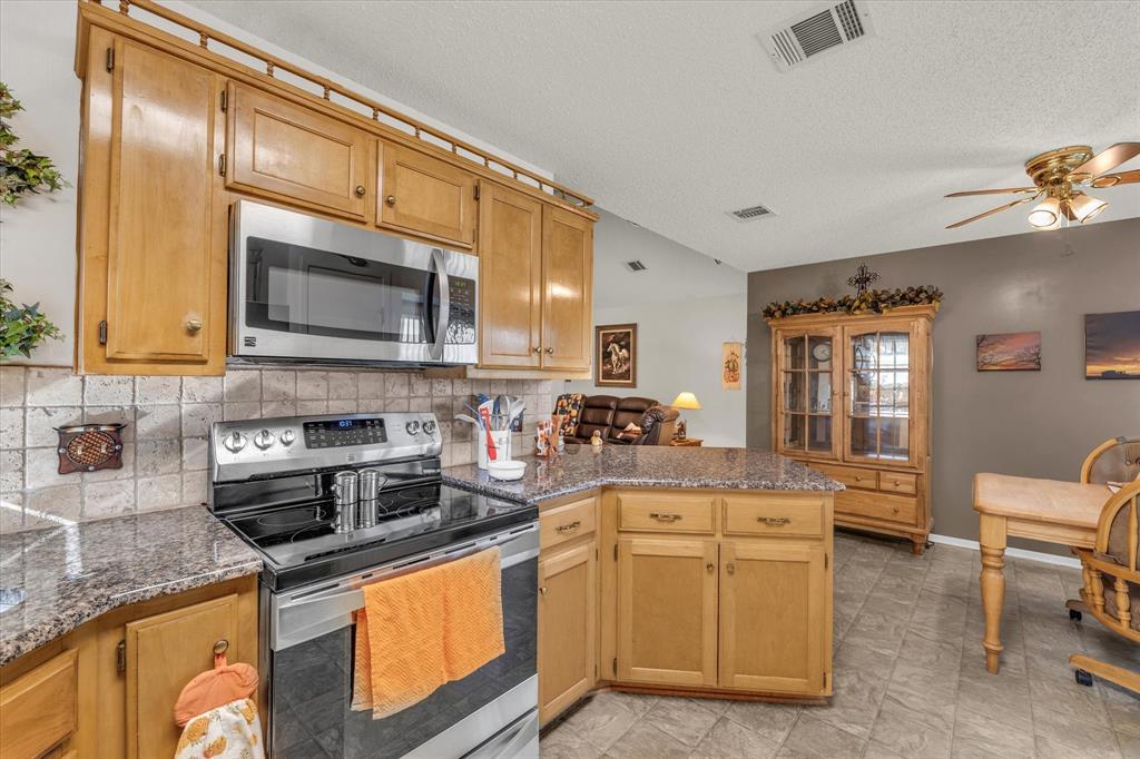 107 Fort Graham Circle Waco, TX 76705 - Photo 12 of 40 Kitchen featuring appliances with stainless steel finishes, backsplash, a peninsula, dark stone countertops, and ceiling fan