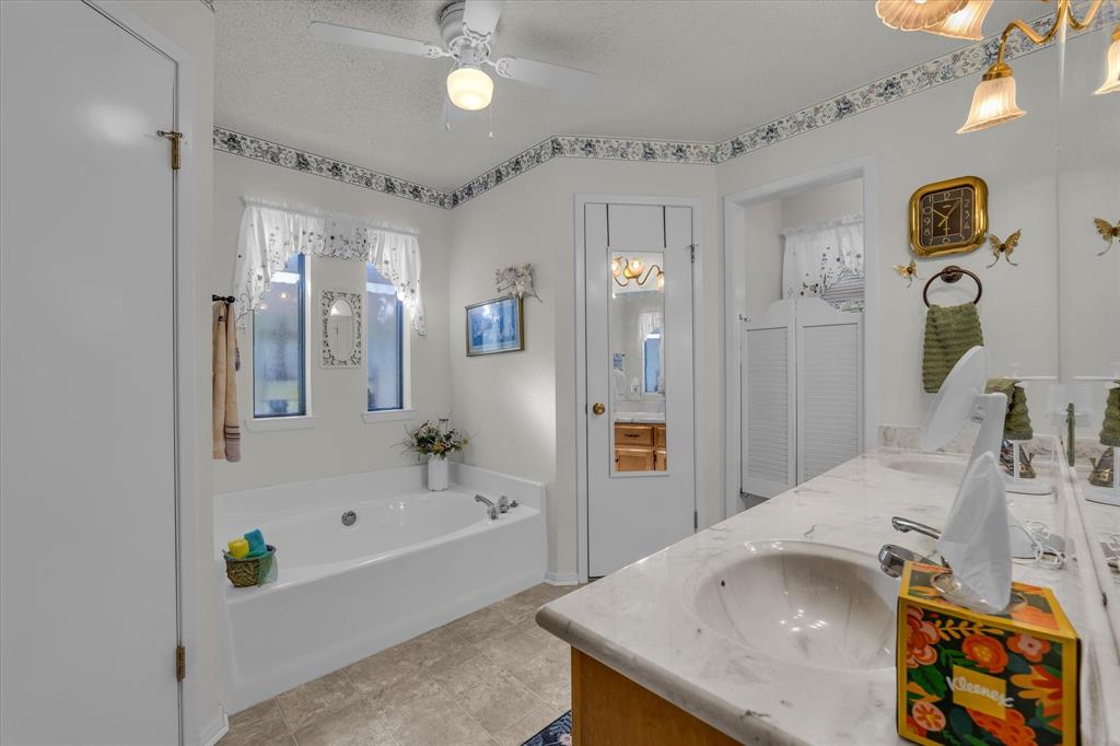 107 Fort Graham Circle Waco, TX 76705 - Photo 18 of 40 Bathroom featuring double vanity, a bath, a textured ceiling, and a ceiling fan