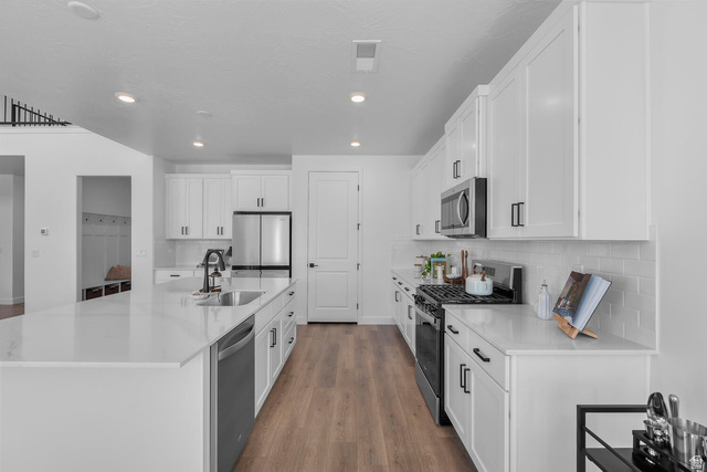 382 North Rhyolite Drive, Unit 111 Hurricane, UT 84737 - Photo 34 of 37 Modern kitchen featuring an expansive island with an undermount sink, white cabinetry, integrated stainless steel appliances, a subway tile backsplash, and wood-finish flooring