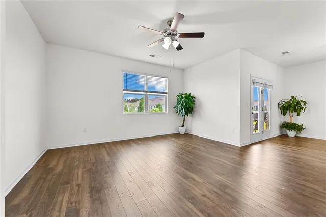 a view of an empty room with wooden floor and a ceiling fan