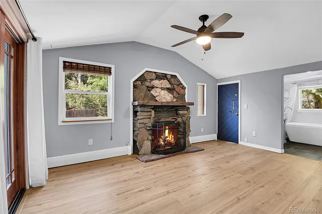 an empty room with wooden floor a fireplace a ceiling fan and a large window