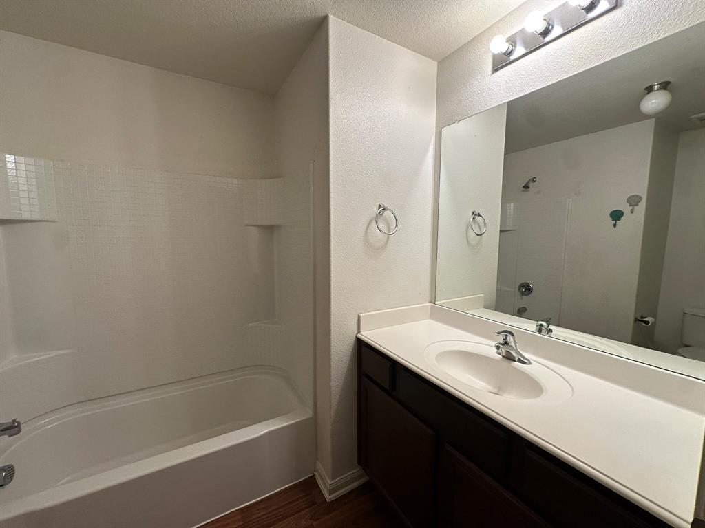 1818 Clegg Street Howe, TX 75459 - Photo 8 of 34 Bathroom featuring a combined shower and tub with built-in shelving, dark wood-finish vanity with an integrated sink and white countertop, and a wall-mounted mirror with overhead bar lighting