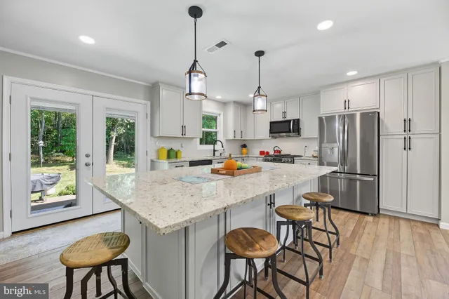 a kitchen with stainless steel appliances granite countertop a refrigerator a sink dishwasher a dining table and chairs with wooden floor