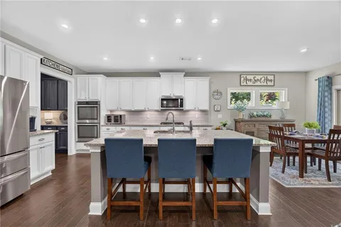 a kitchen with stainless steel appliances granite countertop a dining table chairs refrigerator microwave and cabinets