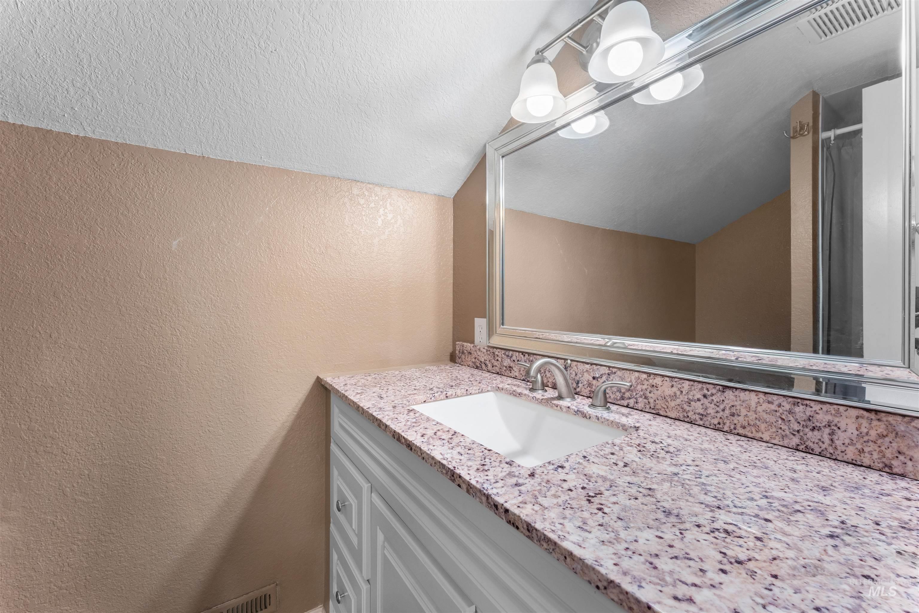 17441 Upper Pleasant Ridge Road Caldwell, ID 83607 - Photo 18 of 40 Bathroom vanity featuring a speckled countertop, integrated white sink, brushed nickel faucet, and a large framed mirror with overhead lighting