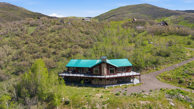 Mountain home featuring a vibrant green metal roof, a full-length covered deck, stone and wood-panel siding, and a prominent stone chimney