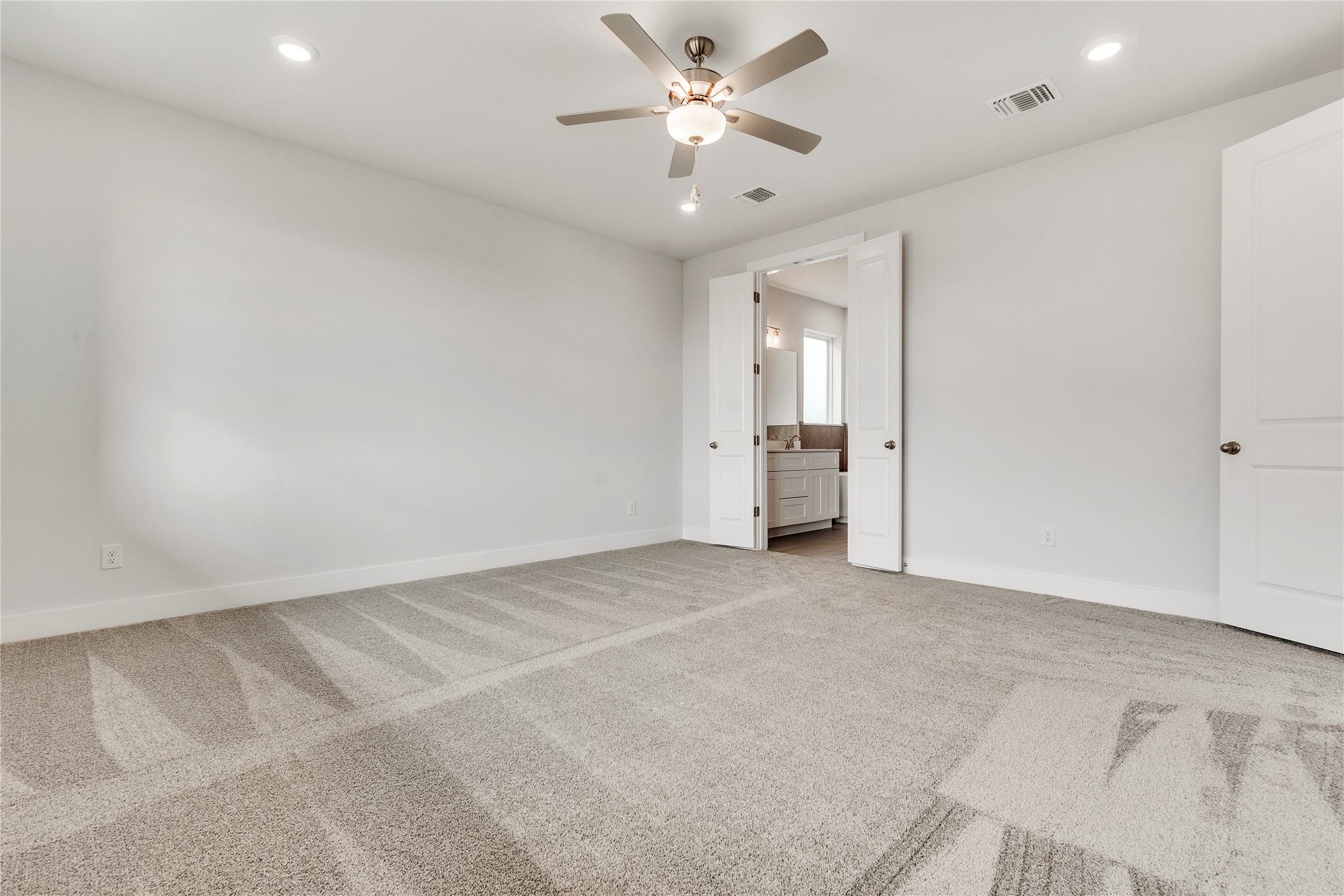 8500 Red Bottle Brush Road Lago Vista, TX 78645 - Photo 17 of 33 A spacious bedroom with plush carpet and direct access to a private bathroom, illuminated by recessed lighting and a ceiling fan.