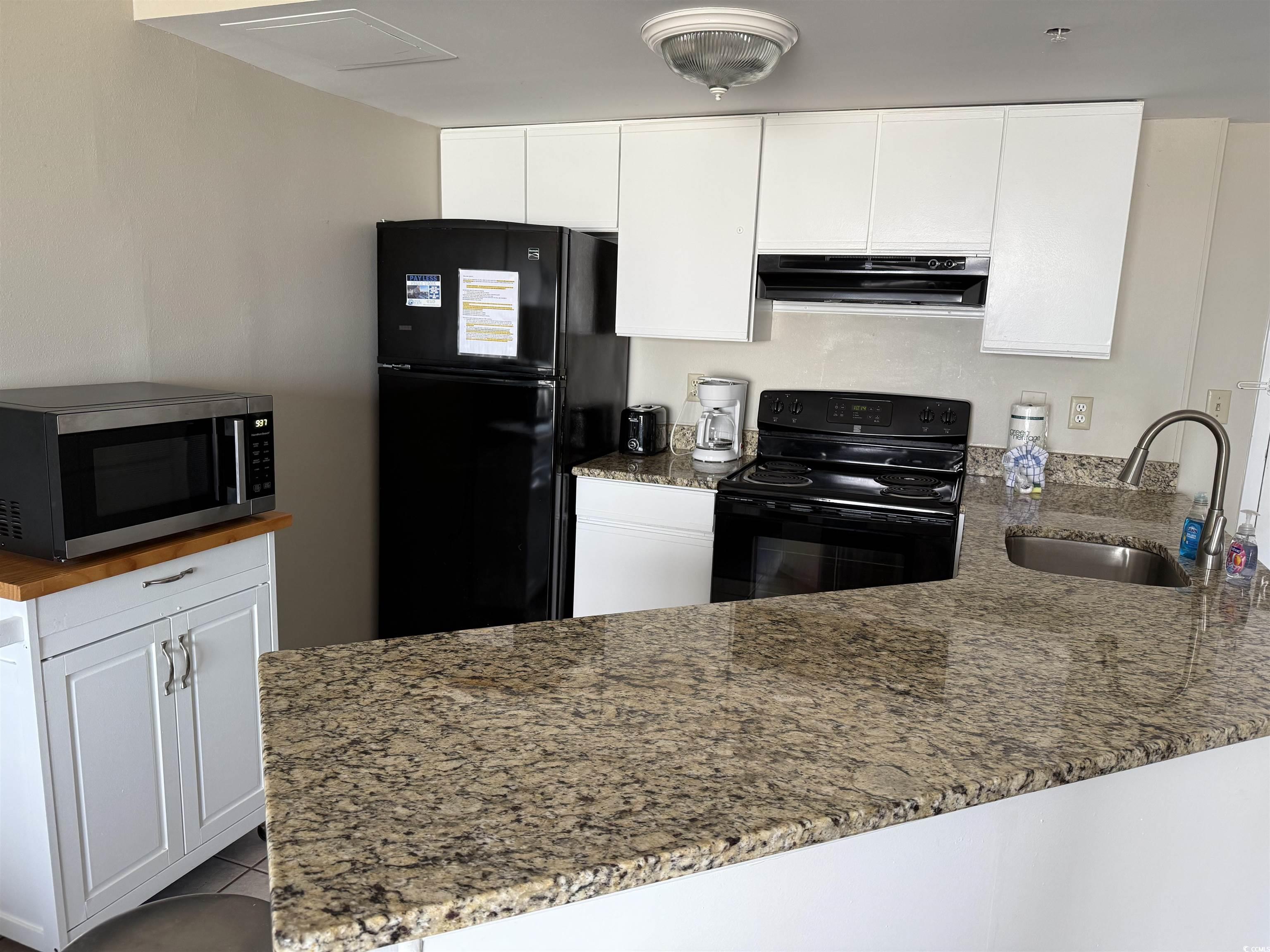 1605 South Ocean Boulevard, Unit 1211 Myrtle Beach, SC 29577 - Photo 5 of 22 Kitchen featuring black appliances, light stone countertops, a peninsula, and white cabinets