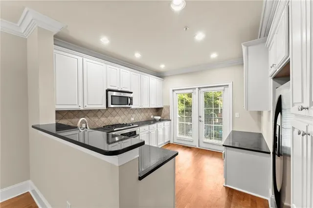 a kitchen with stainless steel appliances granite countertop a refrigerator a stove a sink a microwave a refrigerator and white cabinets with wooden floor