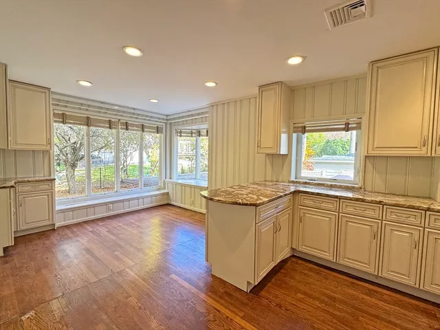 a kitchen with stainless steel appliances granite countertop a stove a sink and white cabinets with wooden floor next to windows