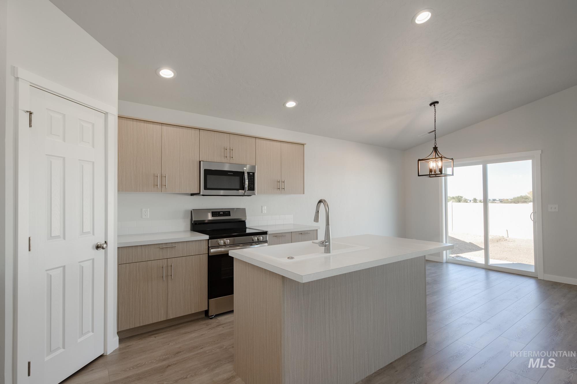 1609 Sunday River Street Middleton, ID 83644 - Photo 4 of 22 Kitchen featuring appliances with stainless steel finishes, light countertops, light brown cabinetry, decorative light fixtures, and a kitchen island with sink