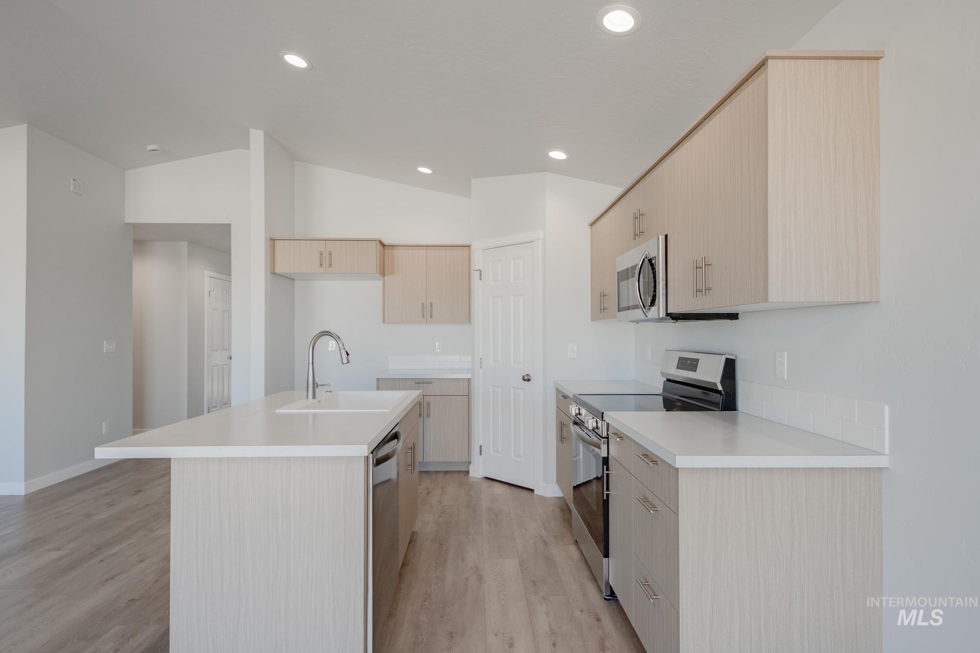 1609 Sunday River Street Middleton, ID 83644 - Photo 7 of 22 Kitchen featuring light brown cabinets, stainless steel appliances, light countertops, a kitchen island with sink, and vaulted ceiling