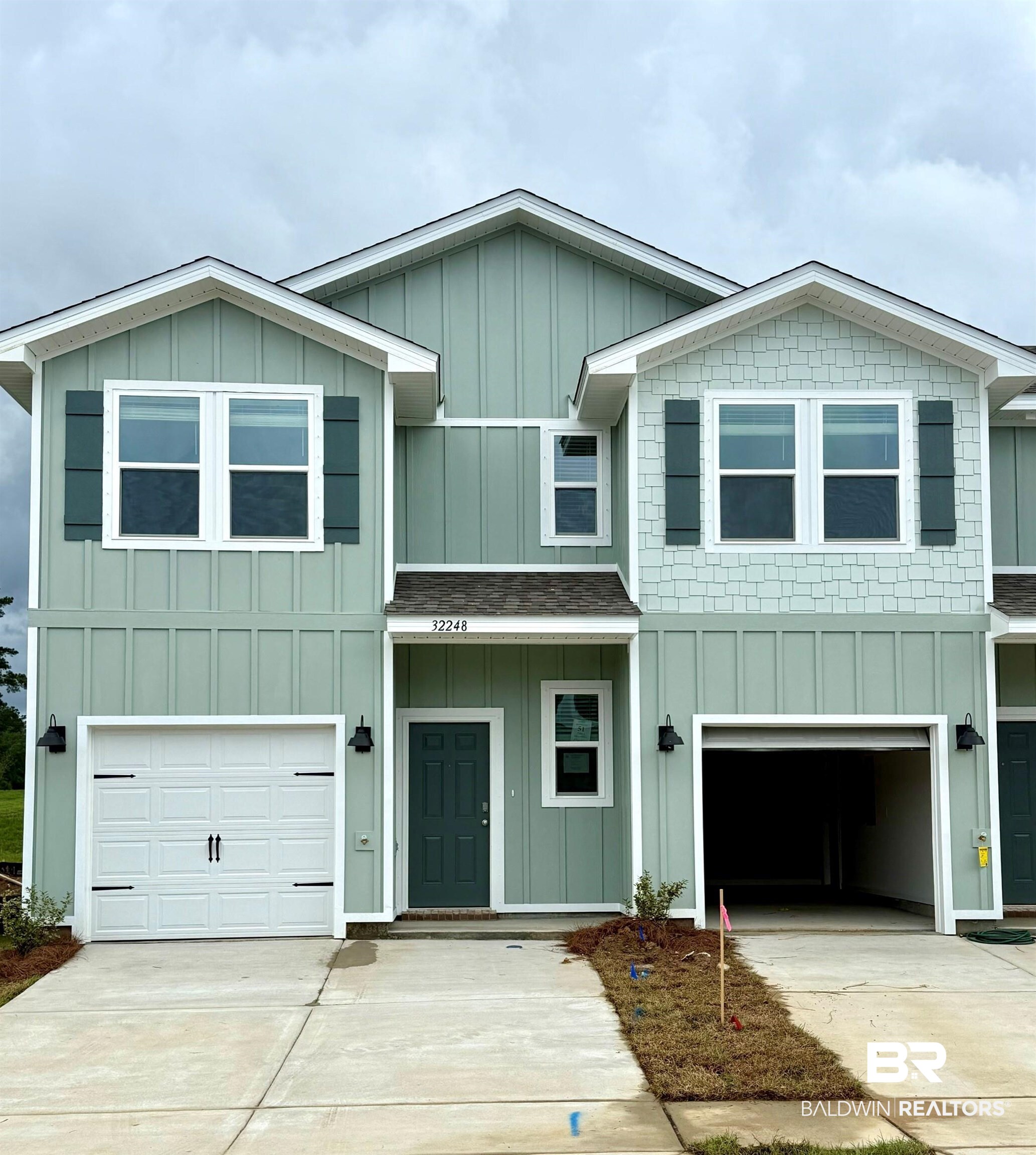 32248 Emancipation Circle Daphne, AL 36527 - Photo 1 of 41 Contemporary townhouse exterior featuring a pastel green facade with board and batten siding, decorative dark green shutters, an attached garage, and a concrete driveway