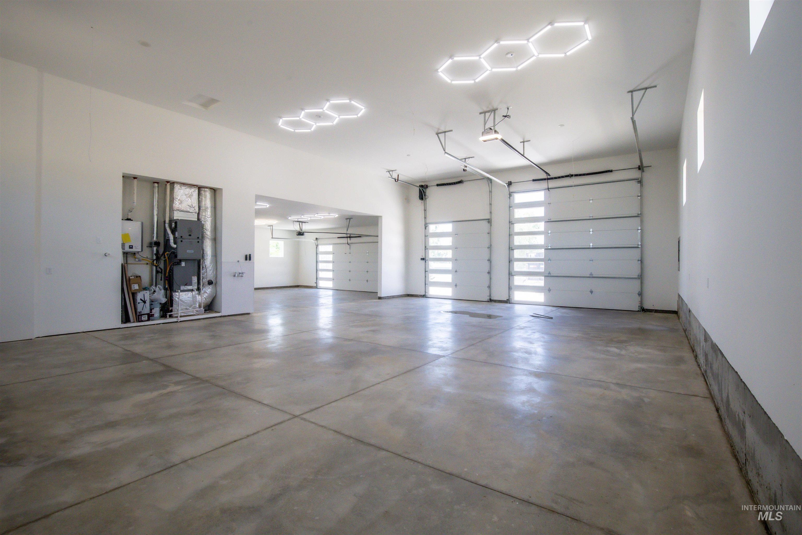 23904 Southview Lane Middleton, ID 83644 - Photo 17 of 29 Spacious garage featuring a concrete floor, multiple segmented overhead doors with frosted glass panels, and modern hexagonal ceiling light fixtures