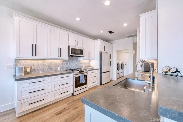 a kitchen with stainless steel appliances granite countertop a stove top oven a sink a refrigerator and white cabinets with wooden floor