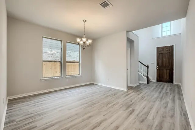 an empty room with wooden floor chandelier and windows