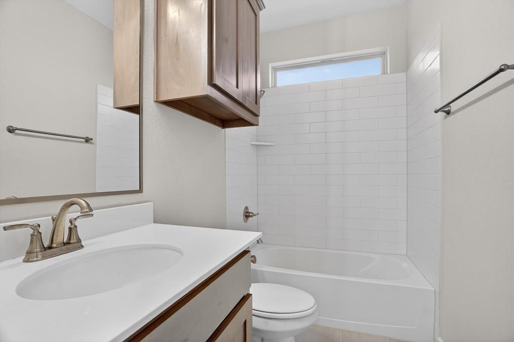 321 Skeen Peak Springtown, TX 76082 - Photo 28 of 37 Bathroom featuring a white bathtub with subway tile surround, single vanity with integrated sink, brushed nickel faucet, and wood-finish cabinetry