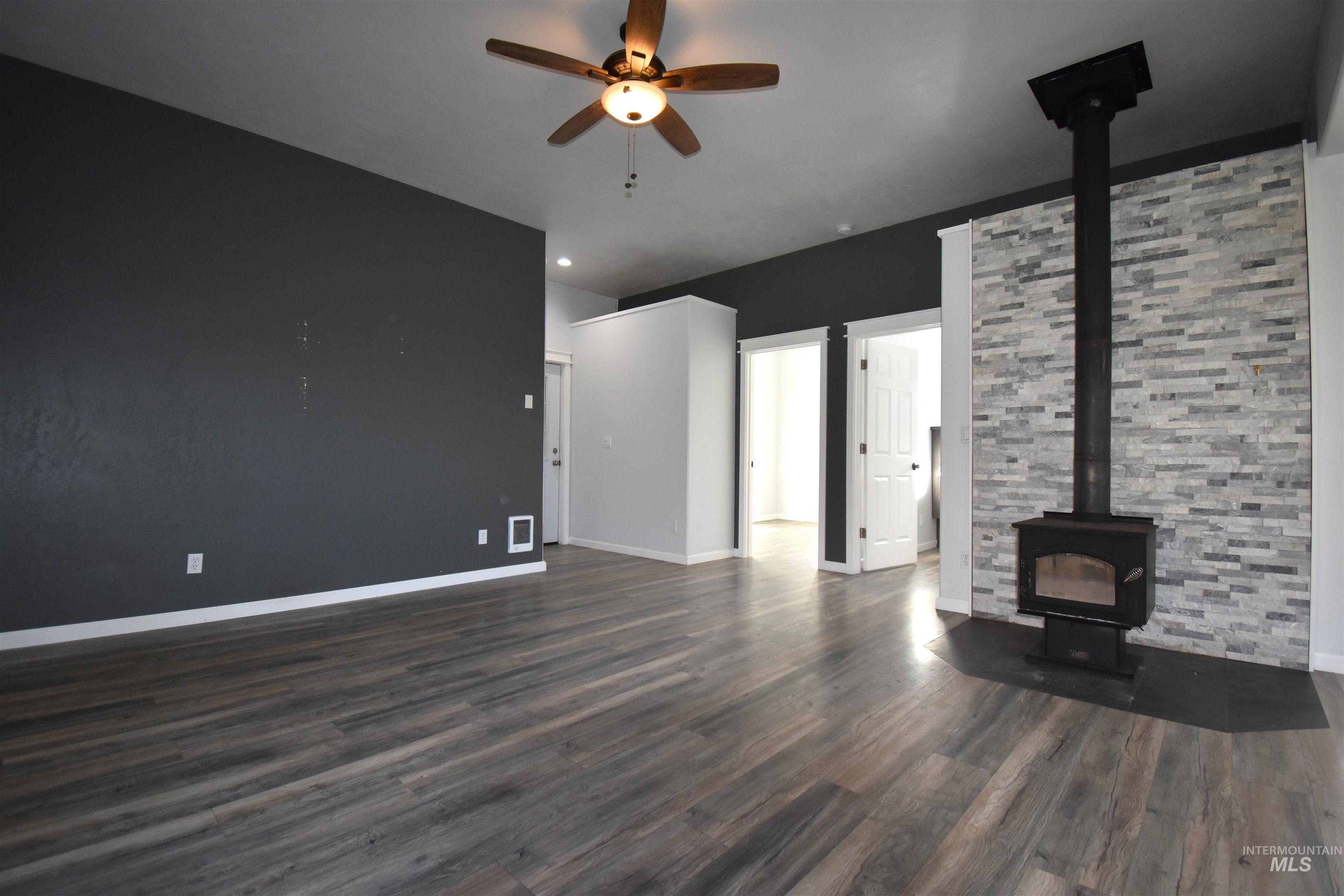 2599 Fruitvale Glendale Road Council, ID 83612 - Photo 2 of 29 Unfurnished living room featuring ceiling fan, dark wood-style flooring, and a wood stove
