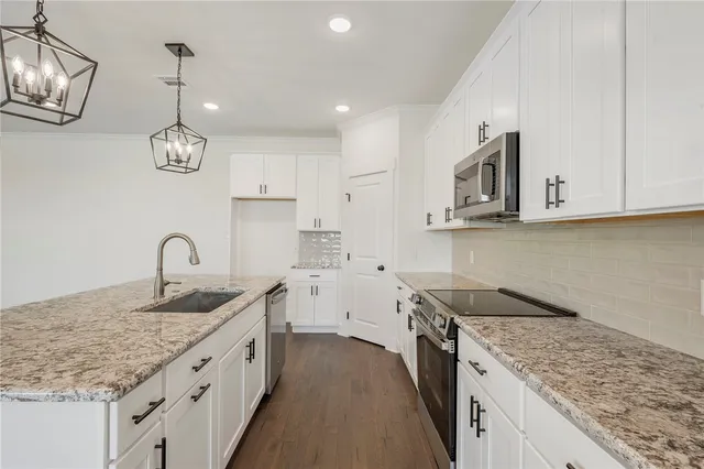 a kitchen with stainless steel appliances granite countertop a sink dishwasher a stove and a microwave oven with white cabinets