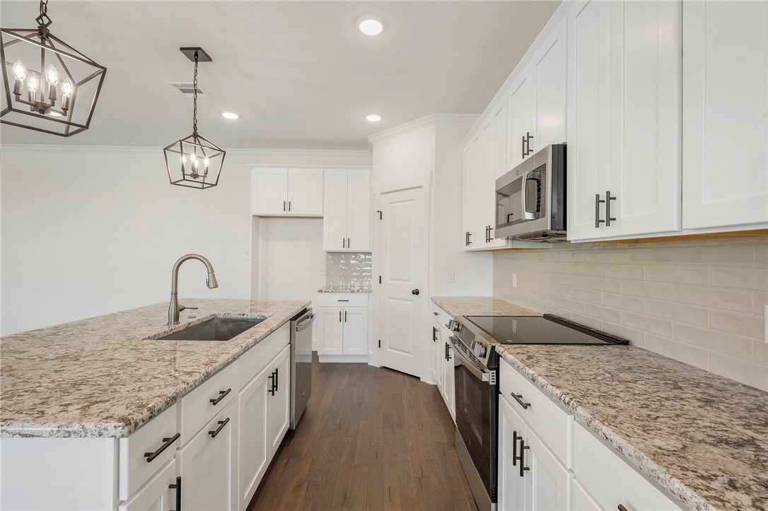 569 Harvest Lk Drive Snook, TX 77879 - Photo 6 of 22 Kitchen featuring appliances with stainless steel finishes, an island with sink, decorative light fixtures, light stone countertops, and crown molding