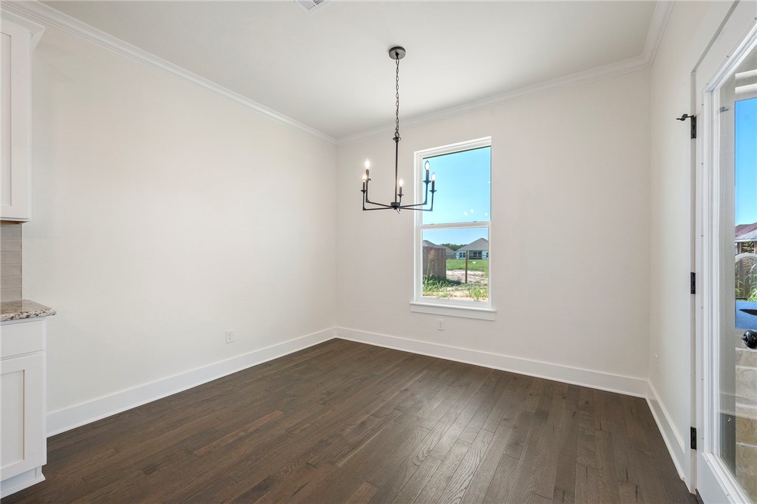 569 Harvest Lk Drive Snook, TX 77879 - Photo 7 of 22 Unfurnished dining area featuring dark wood-type flooring, ornamental molding, and a chandelier