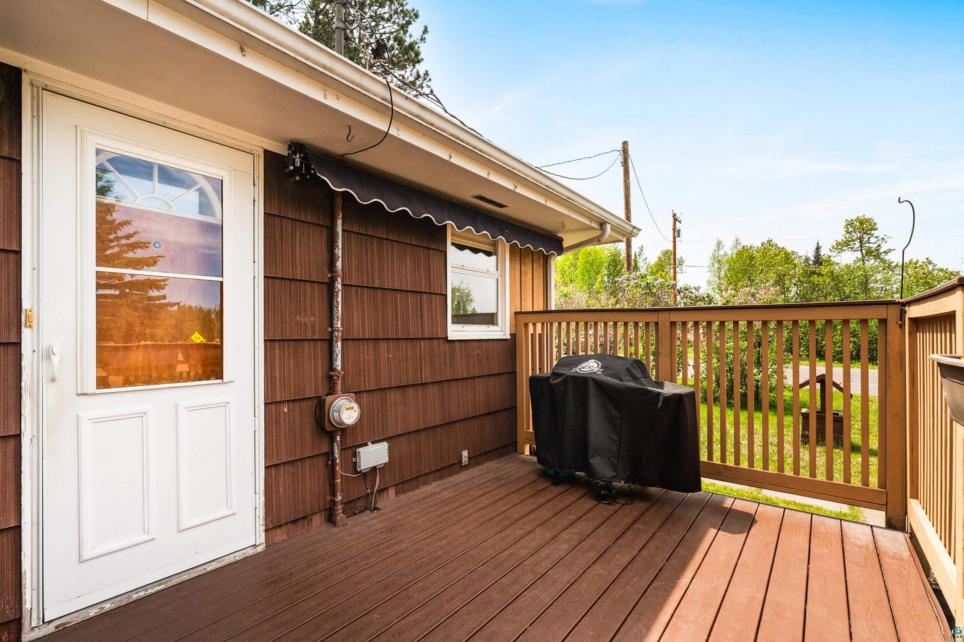 4808 Midway Road Duluth, MN 55811 - Photo 7 of 57 Outdoor deck featuring rich wood-finish flooring, a white glass-paneled entry door, brown shingle siding, a window with a dark awning, and a natural wood railing
