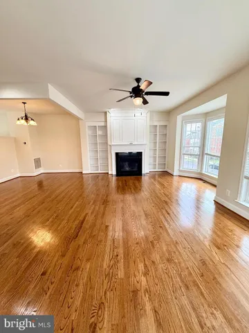 a view of a livingroom with a fireplace a ceiling fan and wooden floor