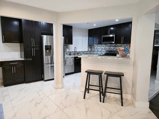 a kitchen with stainless steel appliances kitchen island granite countertop a refrigerator and a sink