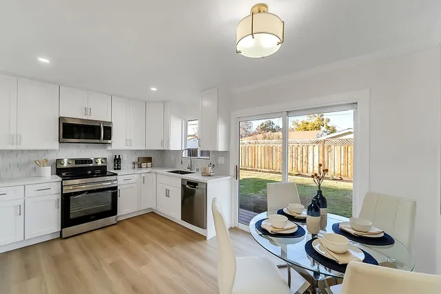 a kitchen with stainless steel appliances granite countertop a stove top oven a sink dishwasher a dining table and chairs with wooden floor