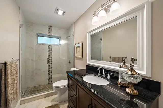 a bathroom with a granite countertop sink a toilet a mirror and shower