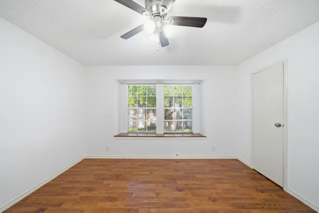 an empty room with wooden floor fan and windows