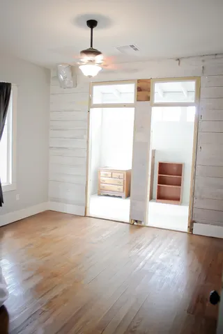 a view of an empty room with wooden floor and fan