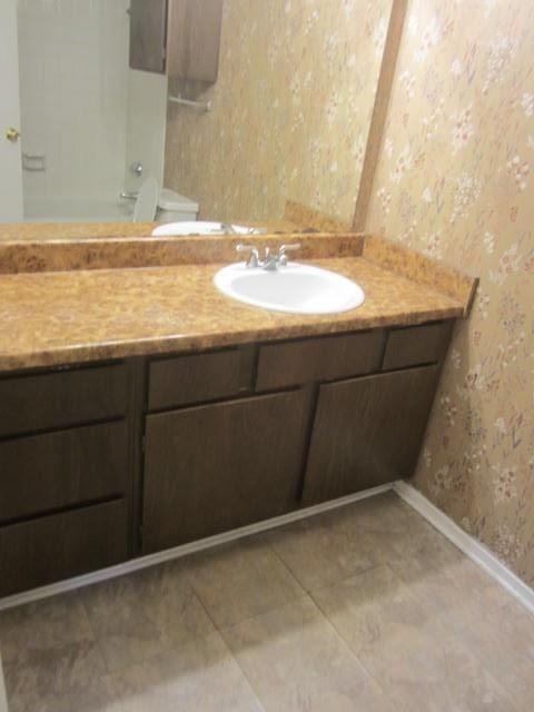 Brown wood-finish vanity with an integrated sink, chrome faucet, and patterned wallpaper