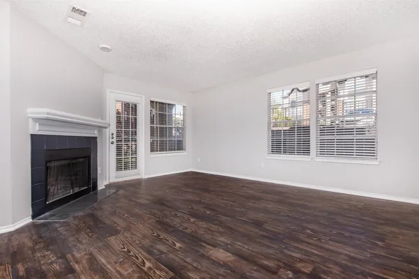 a view of an empty room with wooden floor fireplace and a window