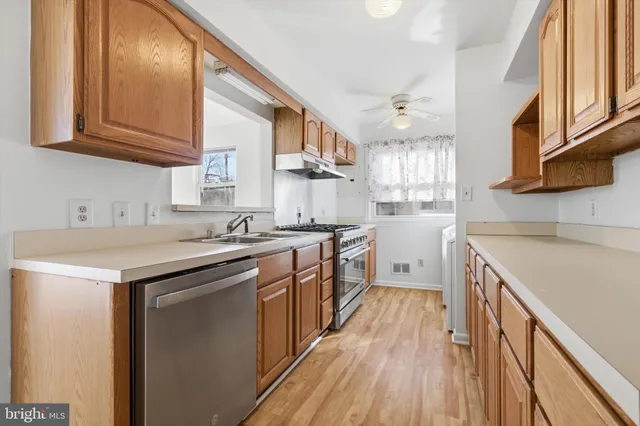 a kitchen with stainless steel appliances granite countertop wooden cabinets a sink a stove a refrigerator and island with wooden floors