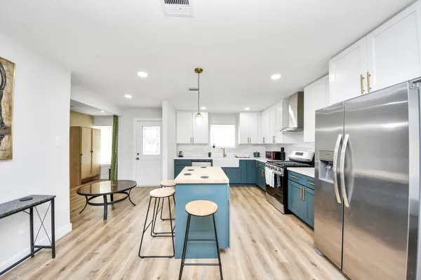 a kitchen with stainless steel appliances kitchen island granite countertop a refrigerator a stove a sink dishwasher and white cabinets with wooden floor
