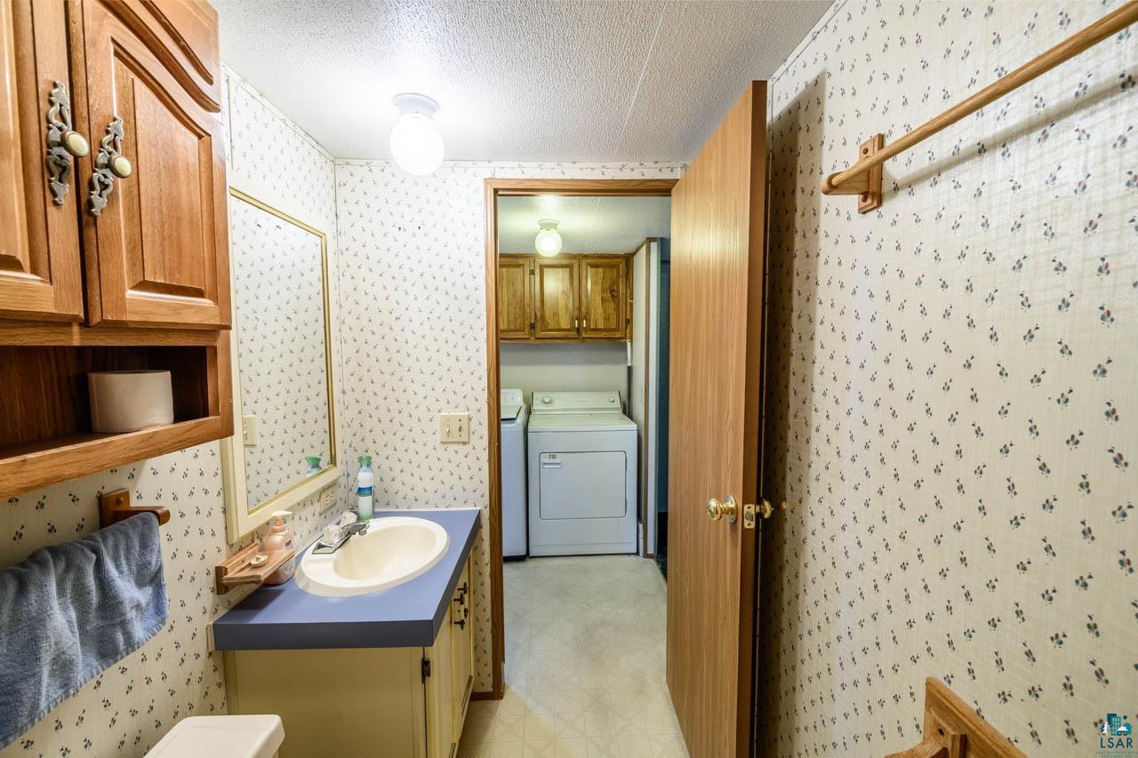 705 4th Street North Biwabik, MN 55708 - Photo 12 of 29 Bathroom featuring a vanity with an oval sink and blue countertop, wood-finish cabinetry, and patterned wallpaper