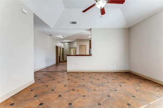 an empty room with a ceiling fan and kitchen view