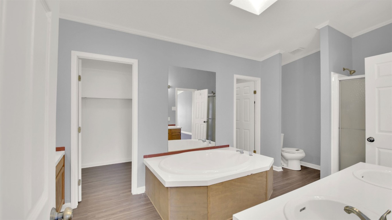 120 Webberwood Way Elgin, TX 78621 - Photo 25 of 36 Bathroom with double vanity, a skylight, a shower stall, a bath, and dark wood-type flooring