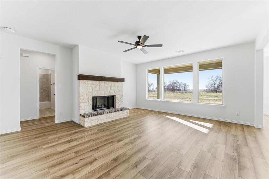 185 Brandywine Trail Rhome, TX 76078 - Photo 13 of 27 Unfurnished living room featuring a fireplace, light wood finished floors, and a ceiling fan