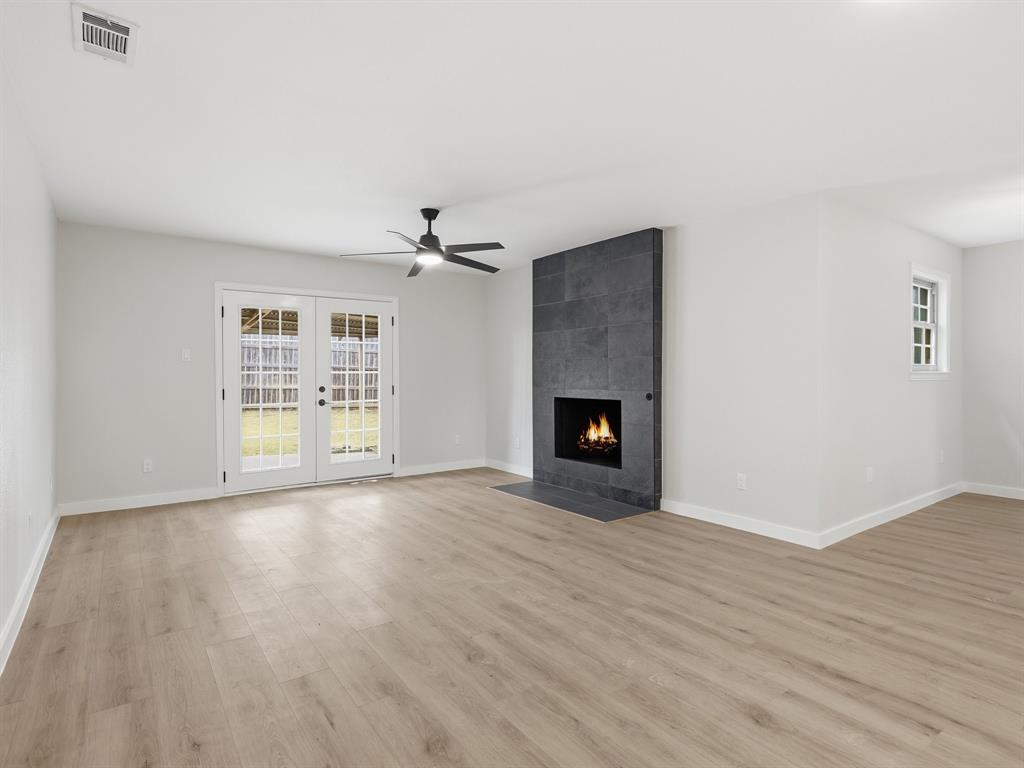 3109 Ridgedale Street Irving, TX 75062 - Photo 4 of 21 Unfurnished living room with light wood-style floors, a tile fireplace, a ceiling fan, and french doors
