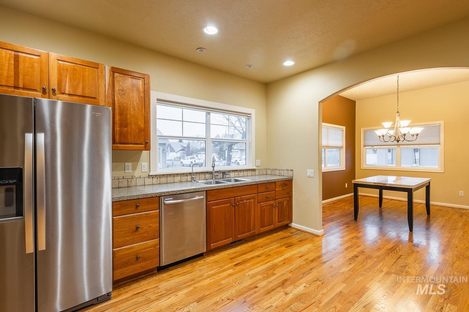 215 South Spring Lake Way Star, ID 83669 - Photo 14 of 50 Kitchen featuring appliances with stainless steel finishes, brown cabinetry, hanging light fixtures, light wood-style flooring, and arched walkways