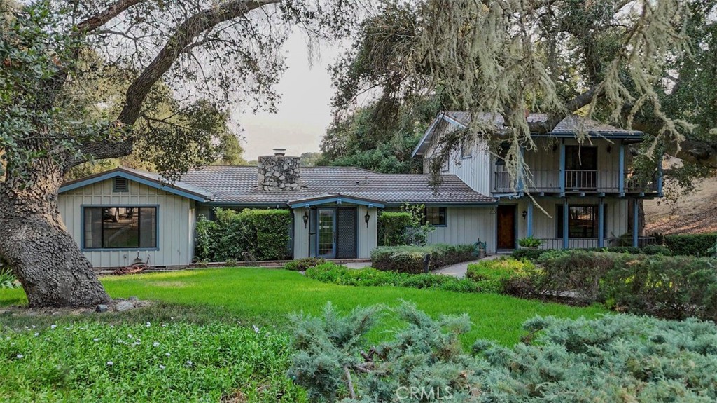 a view of a brick house with a big yard plants and large trees