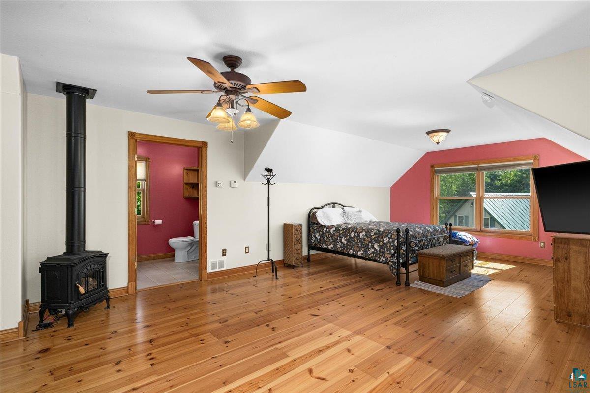 3799 South Lake Road Moose Lake, MN 55767 - Photo 22 of 35 Spacious room featuring wood-finish flooring, a black cast iron stove, and a ceiling fan with integrated lighting