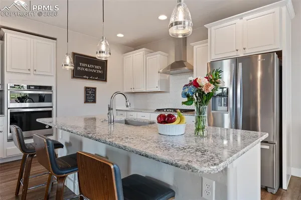 a kitchen with stainless steel appliances granite countertop a dining table chairs refrigerator and sink