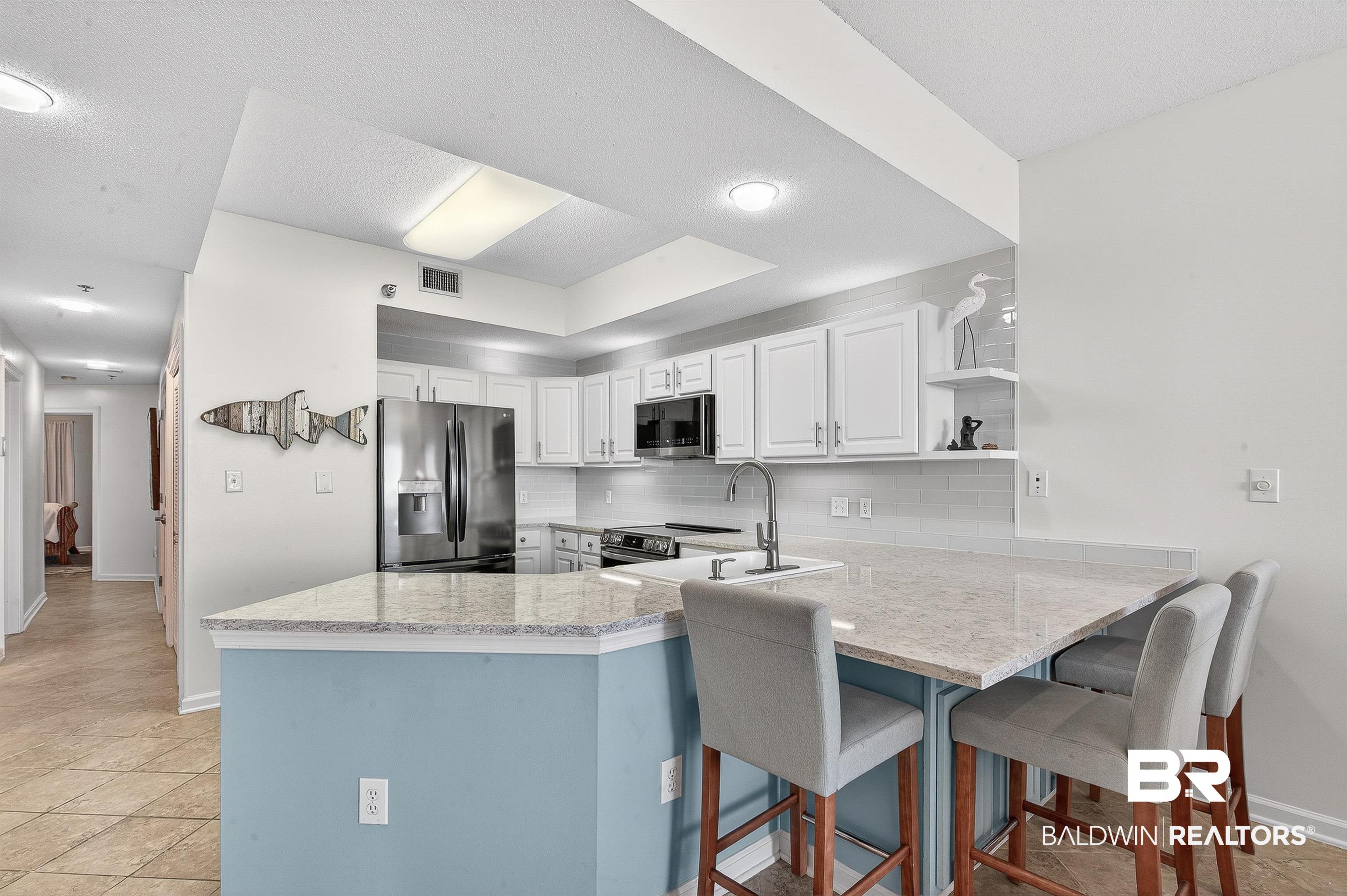 27282 Canal Road, Unit 408 Orange Beach, AL 36561 - Photo 8 of 37 Kitchen featuring tasteful backsplash, open shelves, stainless steel appliances, white cabinetry, and a breakfast bar